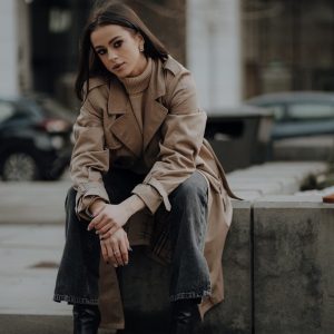 a woman in a trench coat sitting on a curb