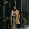 woman in brown coat standing near black metal gate during daytime